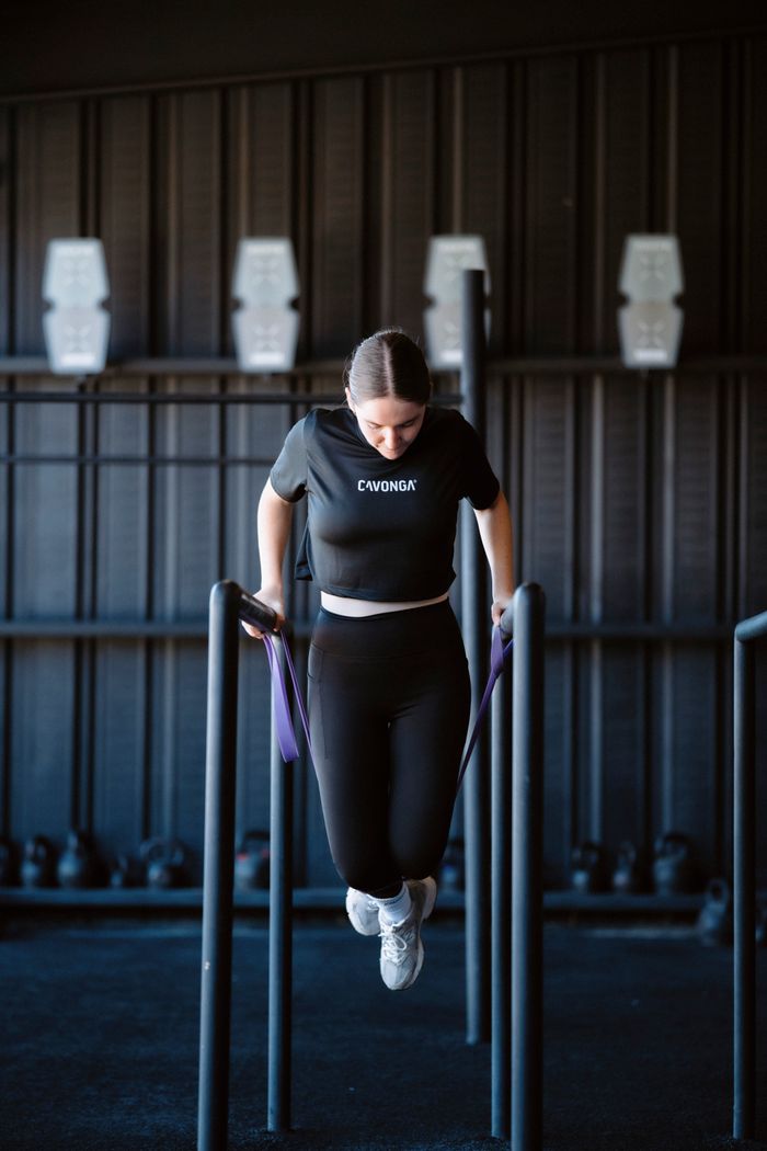 A young woman in a gym uses resistance bands for strength training exercise on parallel bars.